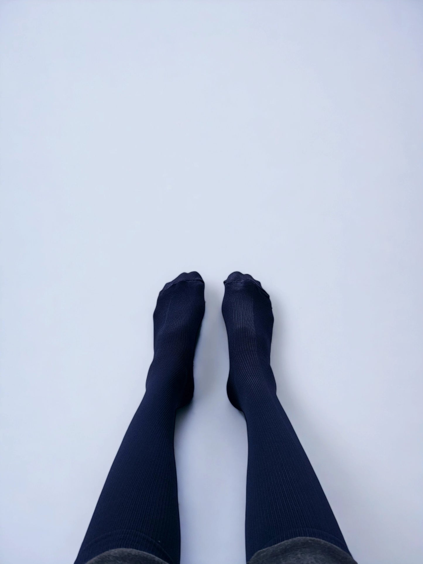 Two legs wearing navy blue graduated compression socks facing upwards.