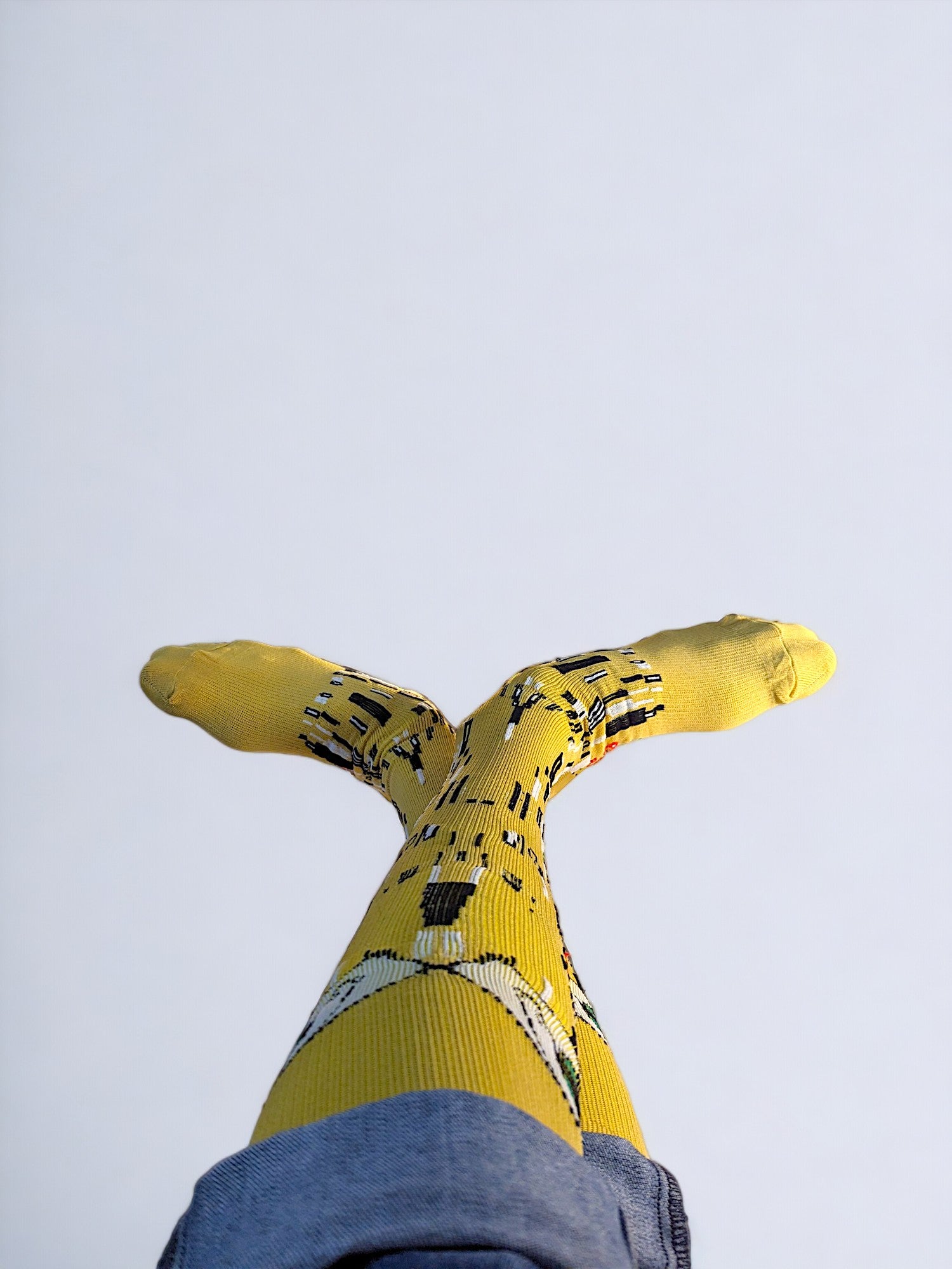 A pair of crossed legs wearing yellow compression socks with the famous painting 'Kiss' printed on it.