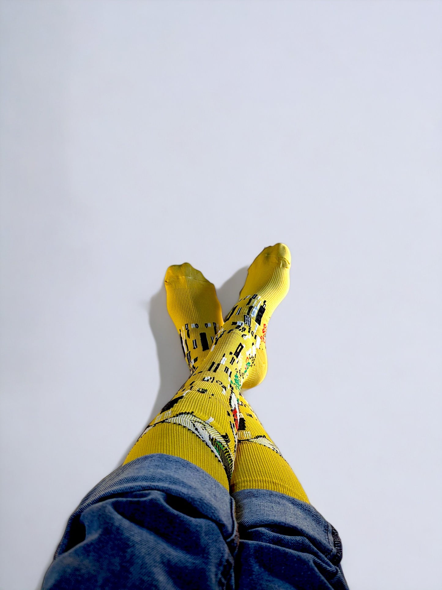A pair of crossed legs wearing yellow compression socks with the famous painting 'Kiss' printed on it.
