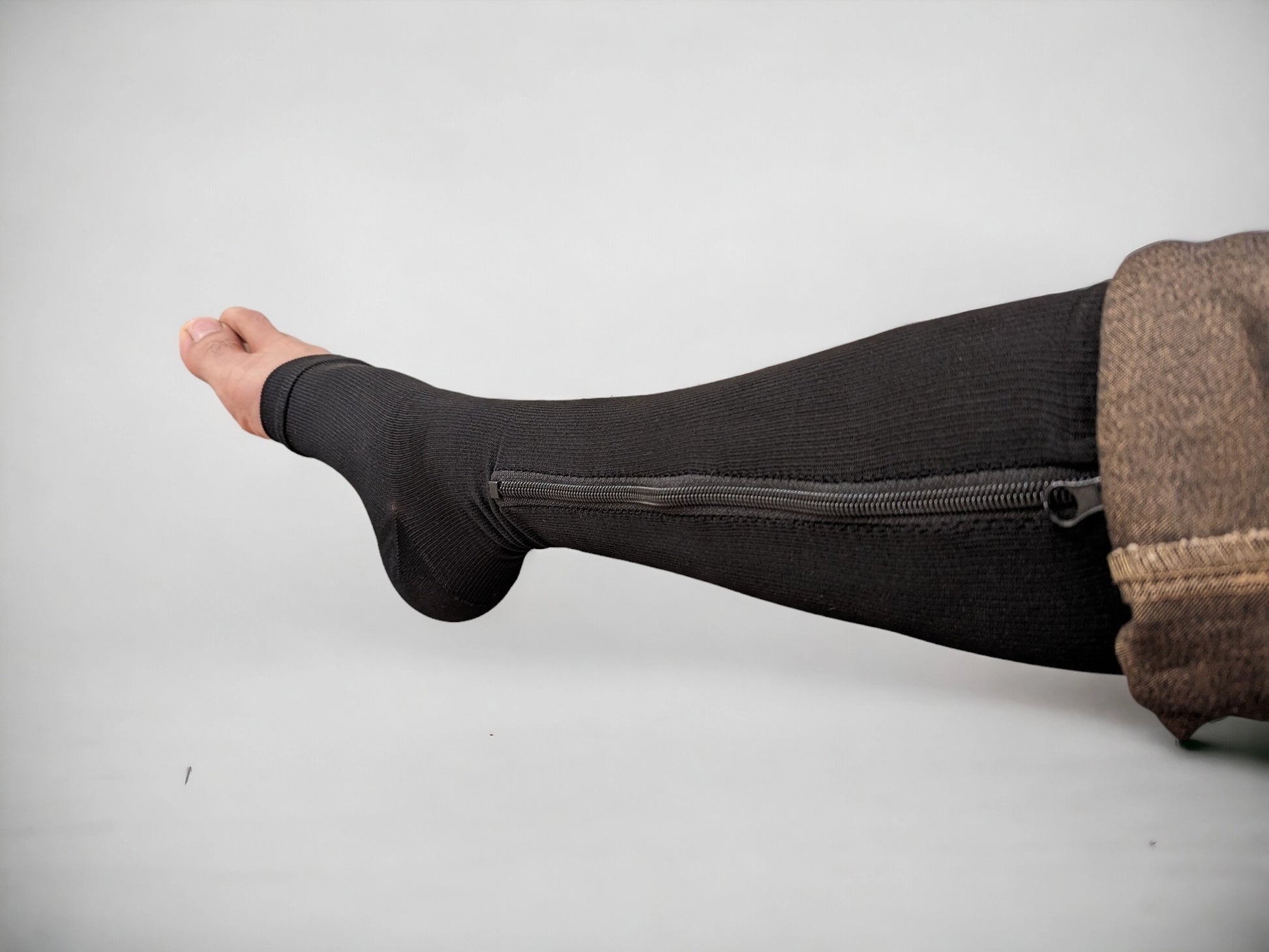 A leg wearing black colored knee-high zippered compression socks