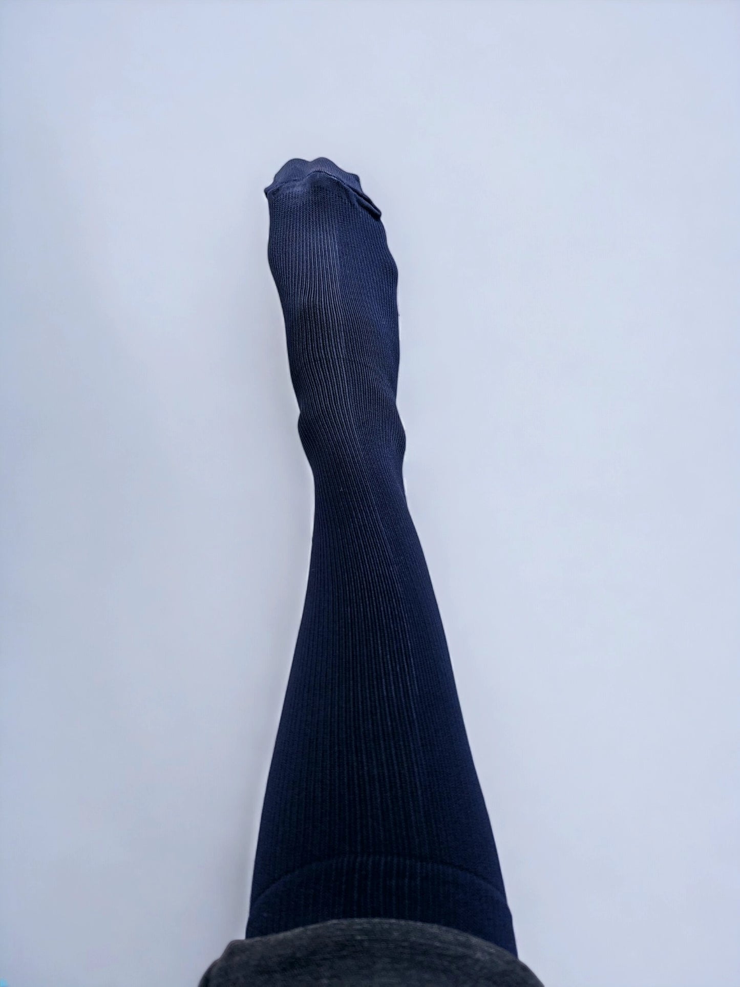 A leg wearing navy blue graduated compression socks raised upwards.