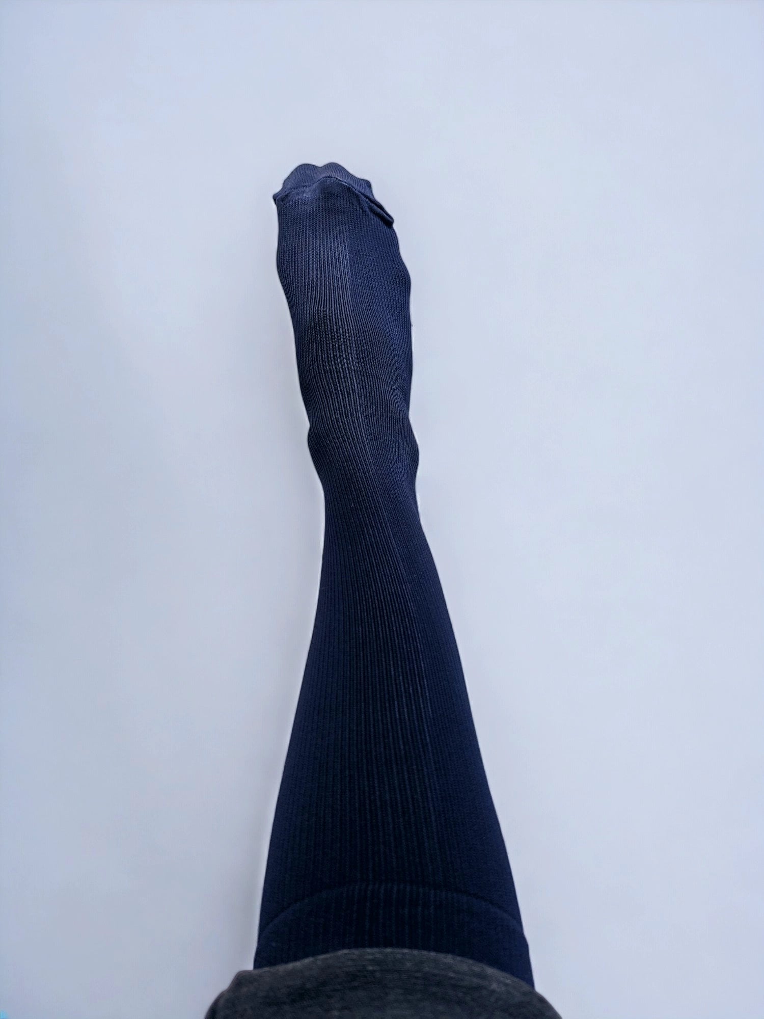 A leg wearing navy blue graduated compression socks raised upwards.