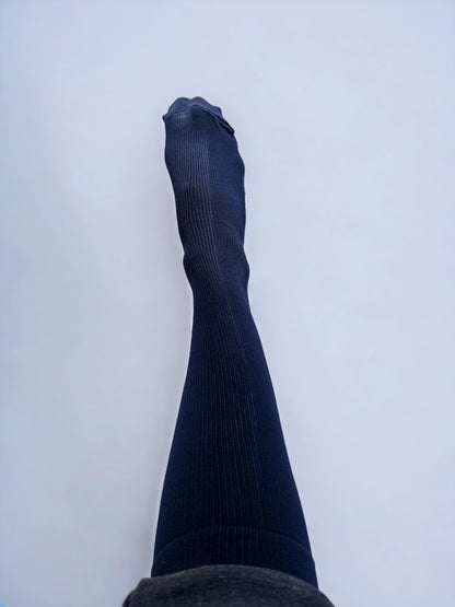 A leg wearing navy blue graduated compression socks raised upwards.