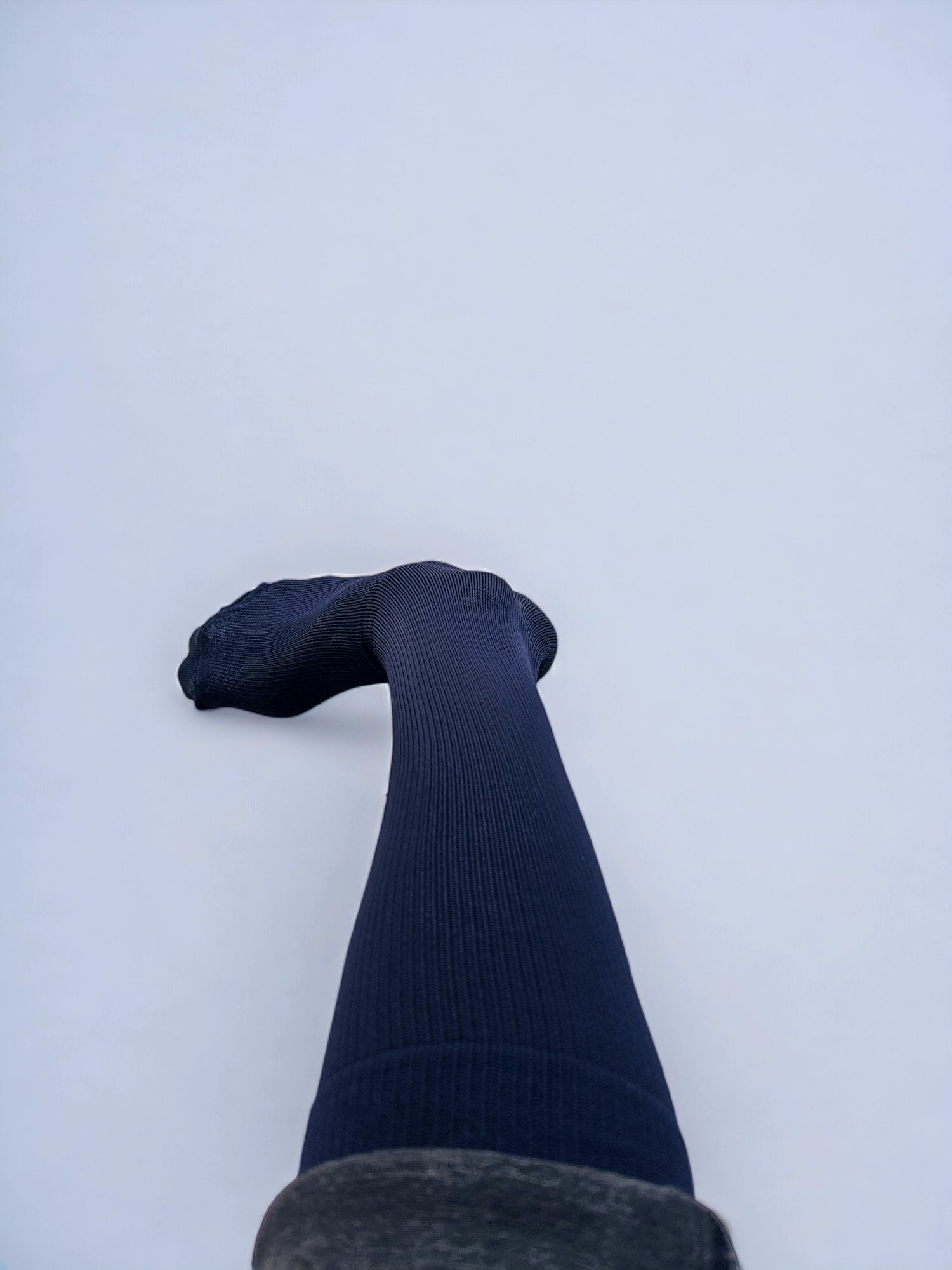 A leg wearing navy blue graduated compression socks turned sideways.