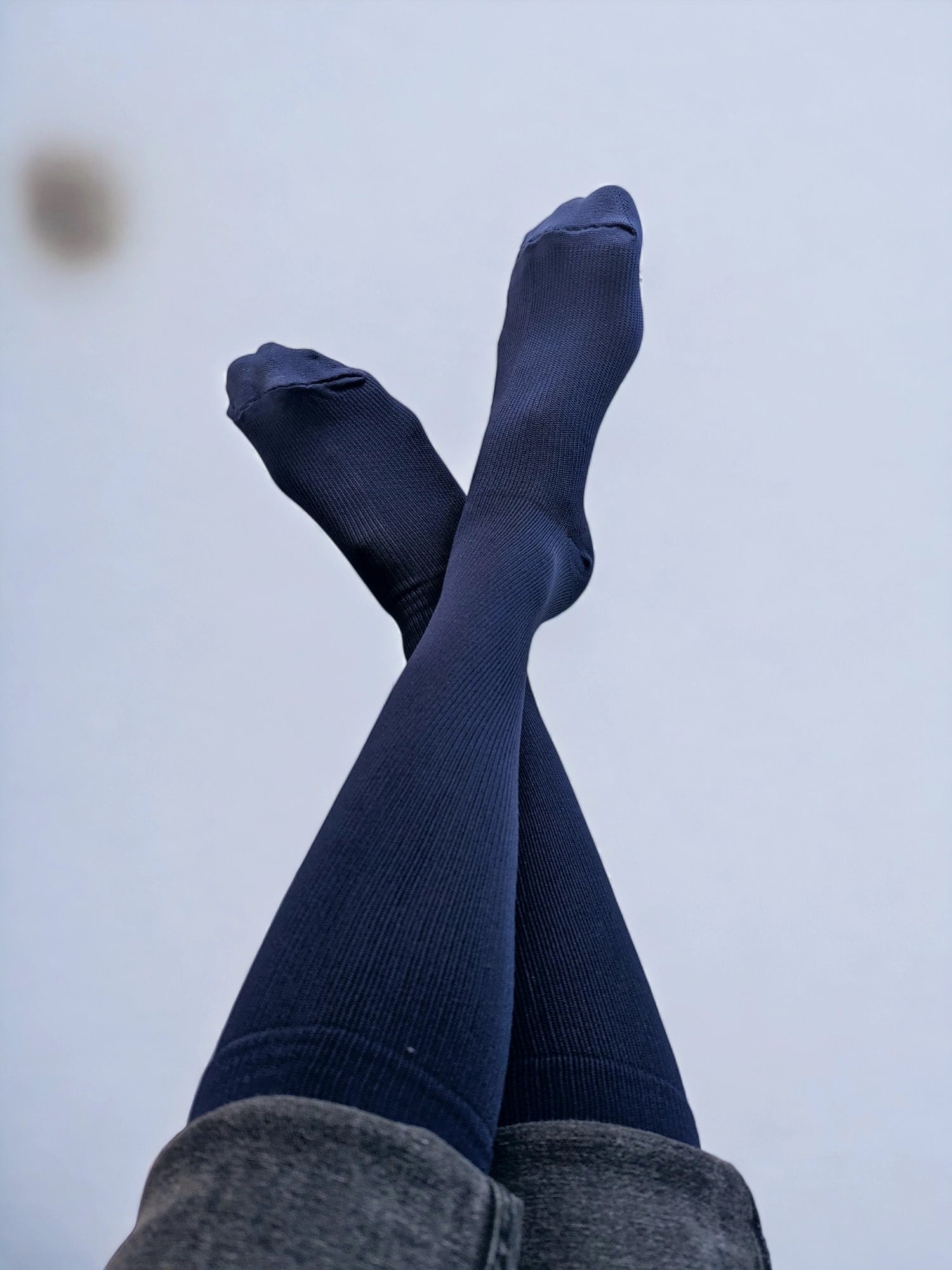 Two legs wearing navy blue graduated compression socks crossed over each other 