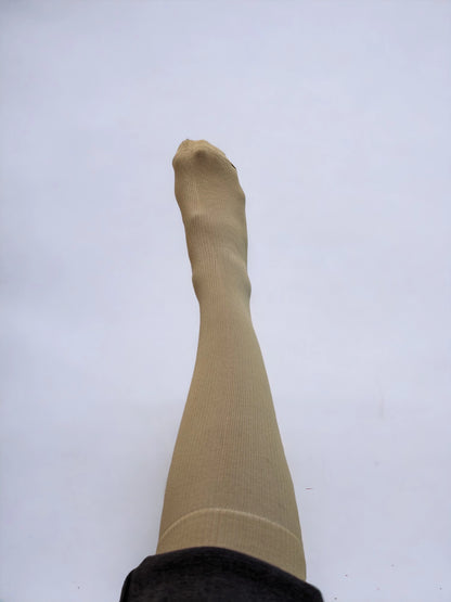 A leg wearing skin-colored compression socks raised upward.