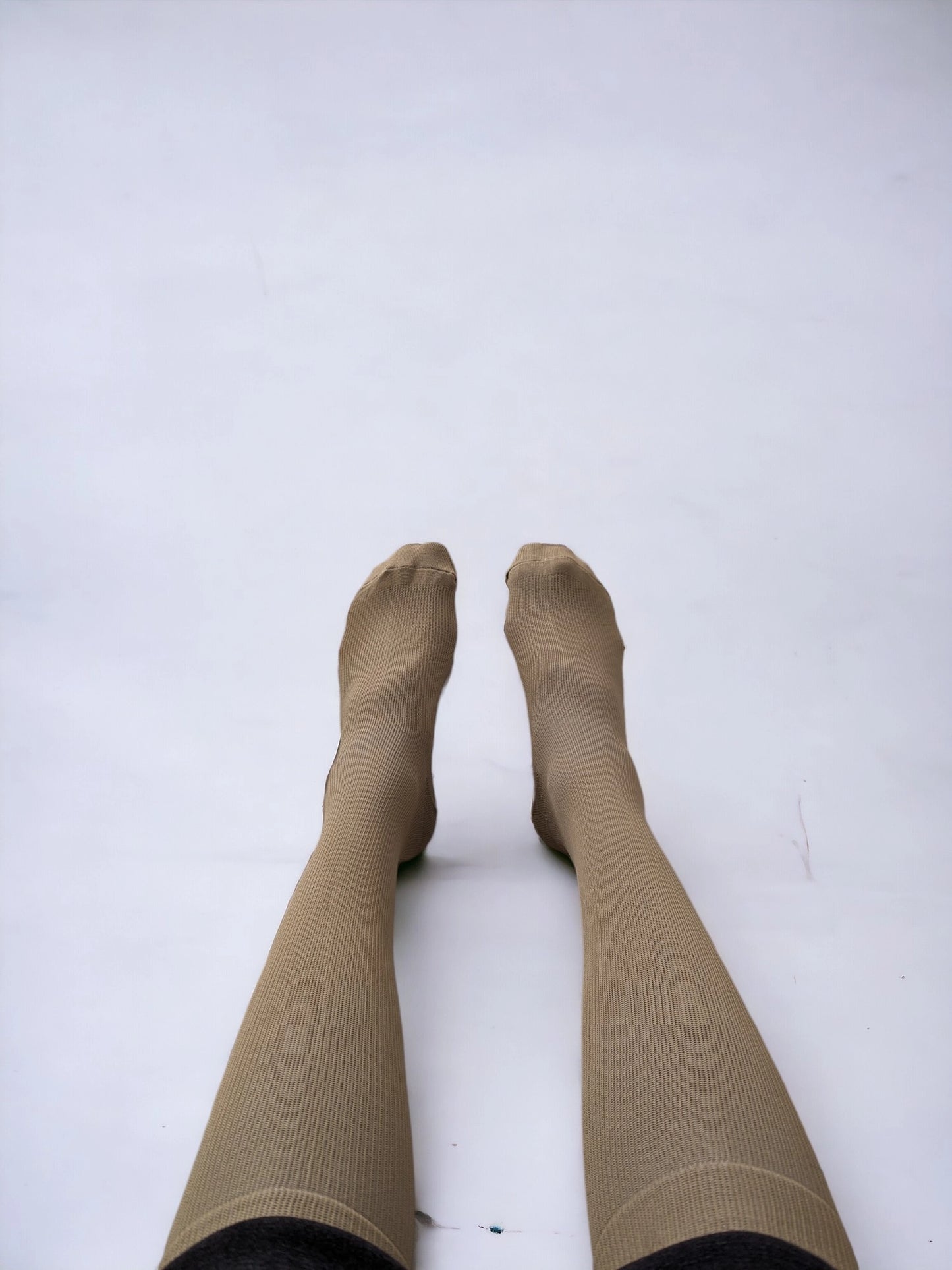 A pair of legs wearing skin-colored compression socks lying on the ground