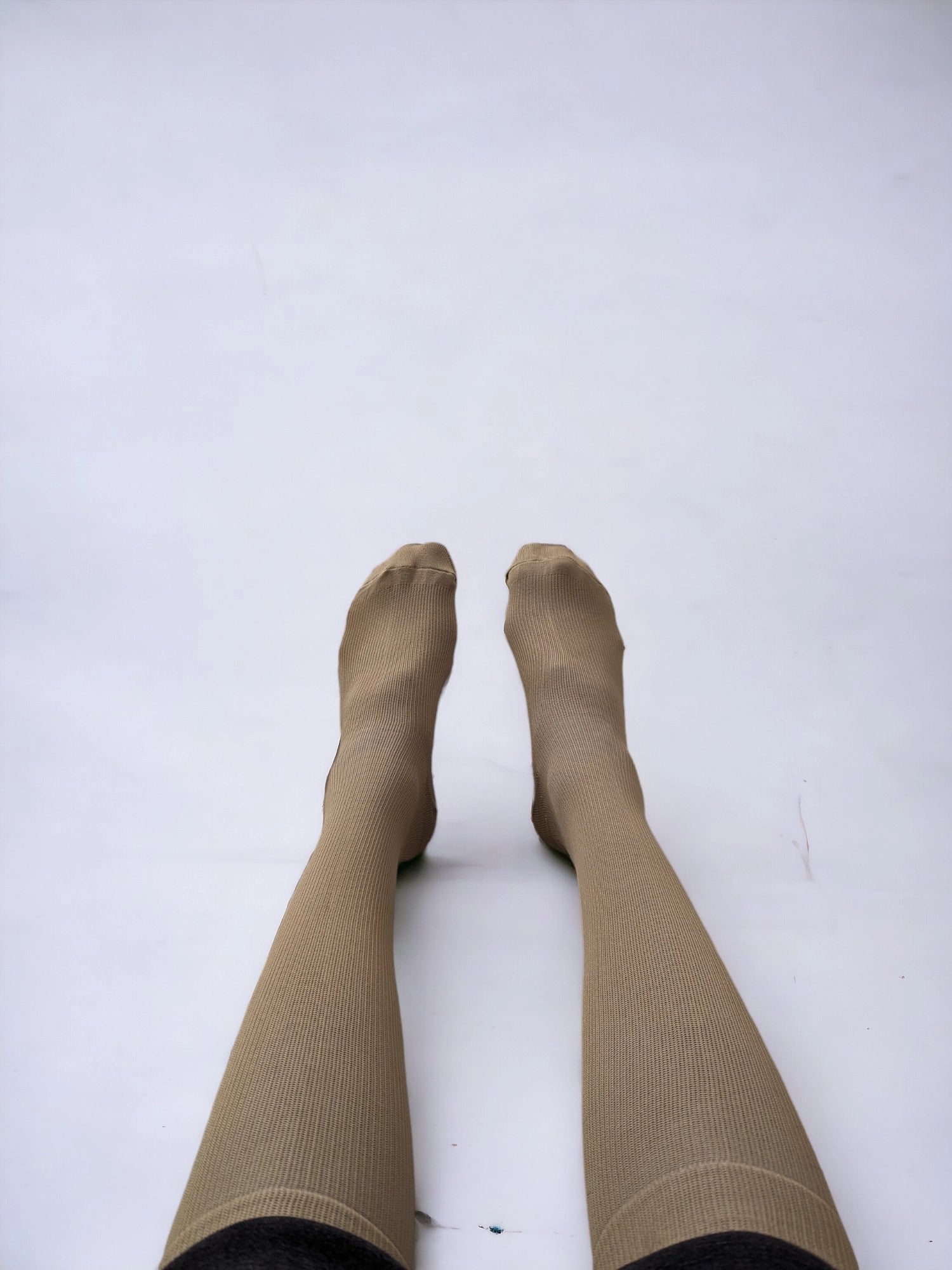A pair of legs wearing skin-colored compression socks lying on the ground