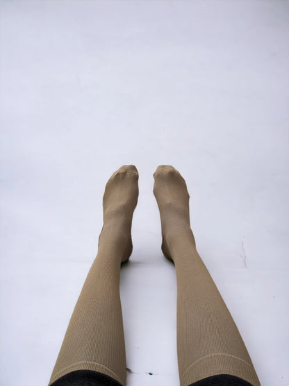 A pair of legs wearing skin-colored compression socks lying on the ground