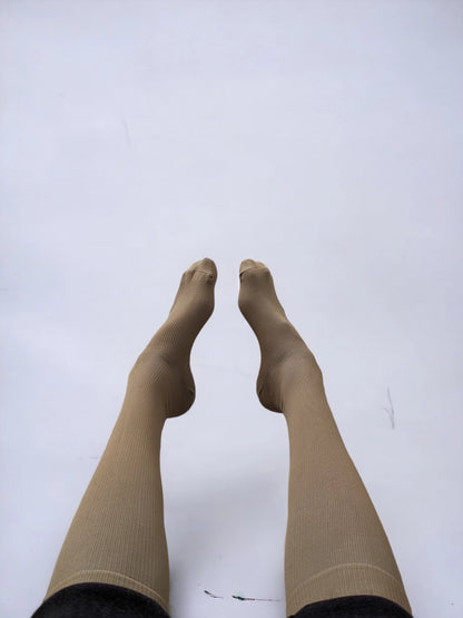 A pair of legs wearing skin-colored compression socks facing each other