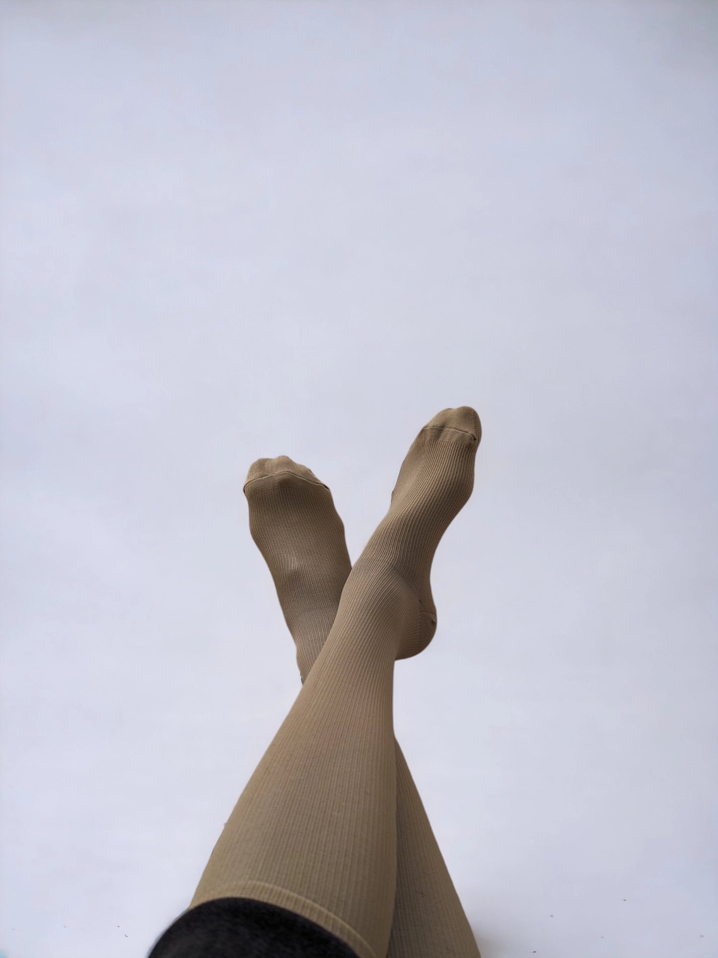 A pair of legs wearing skin-colored compression socks crossed over each other
