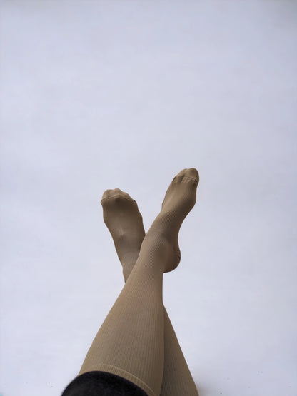 A pair of legs wearing skin-colored compression socks crossed over each other