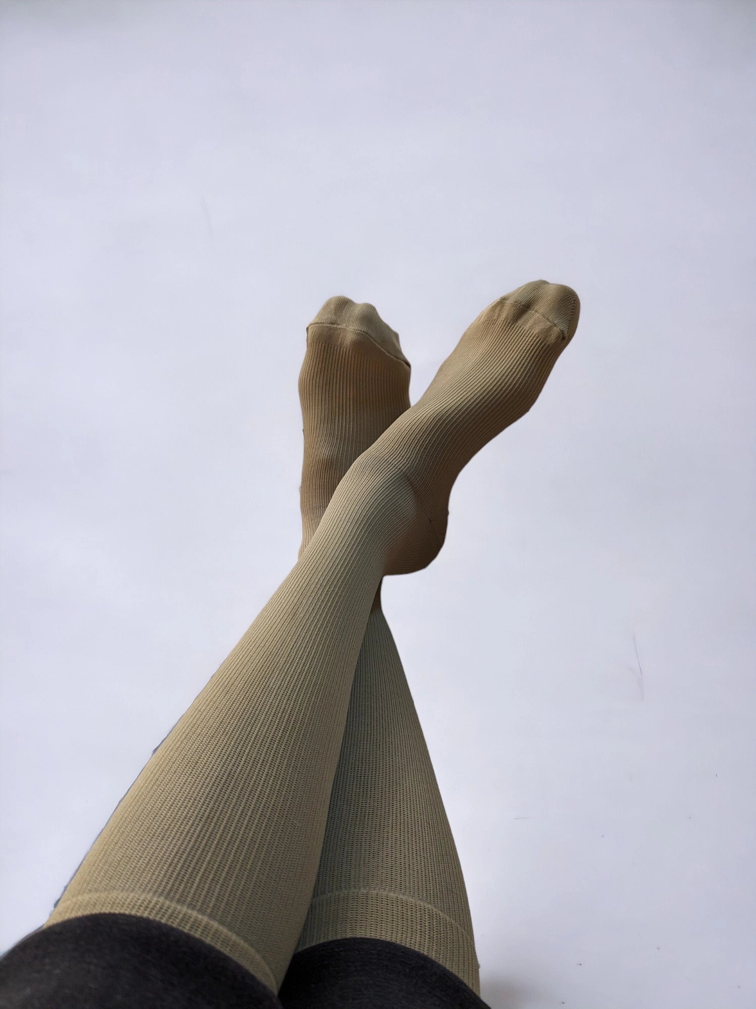A pair of legs wearing skin-colored compression socks crossed over each other