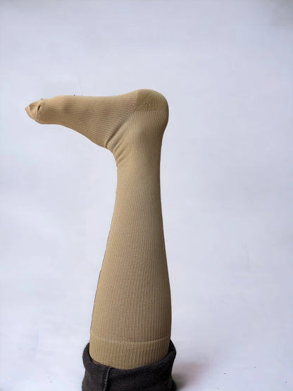 A leg wearing skin-colored compression socks raised upward pointing to left