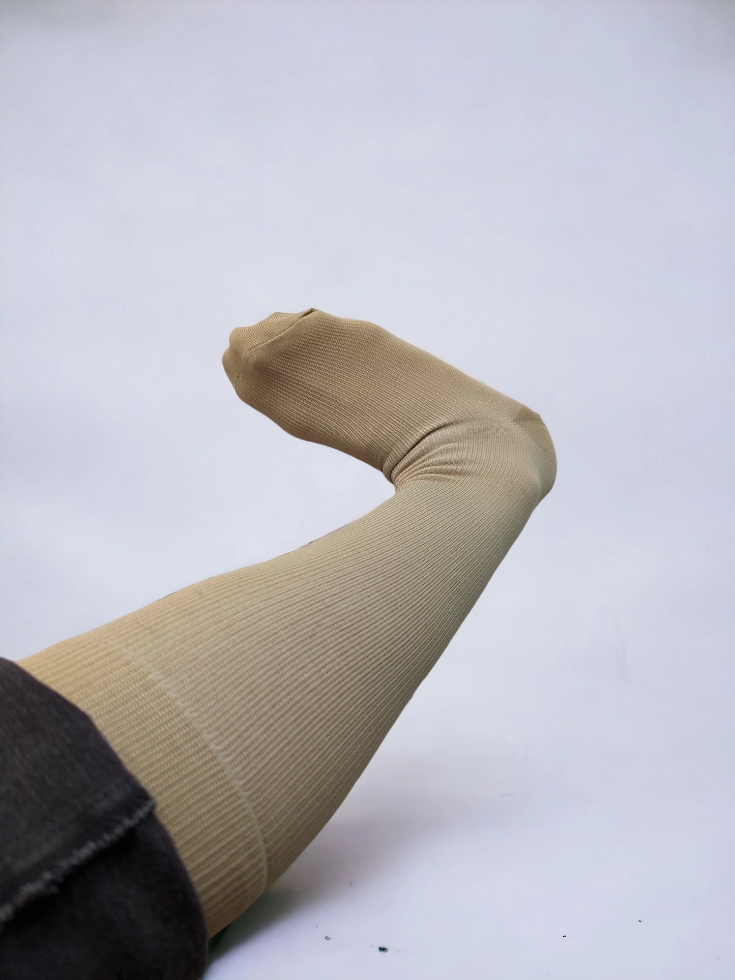 A leg wearing skin-colored compression socks raised upward pointing to left