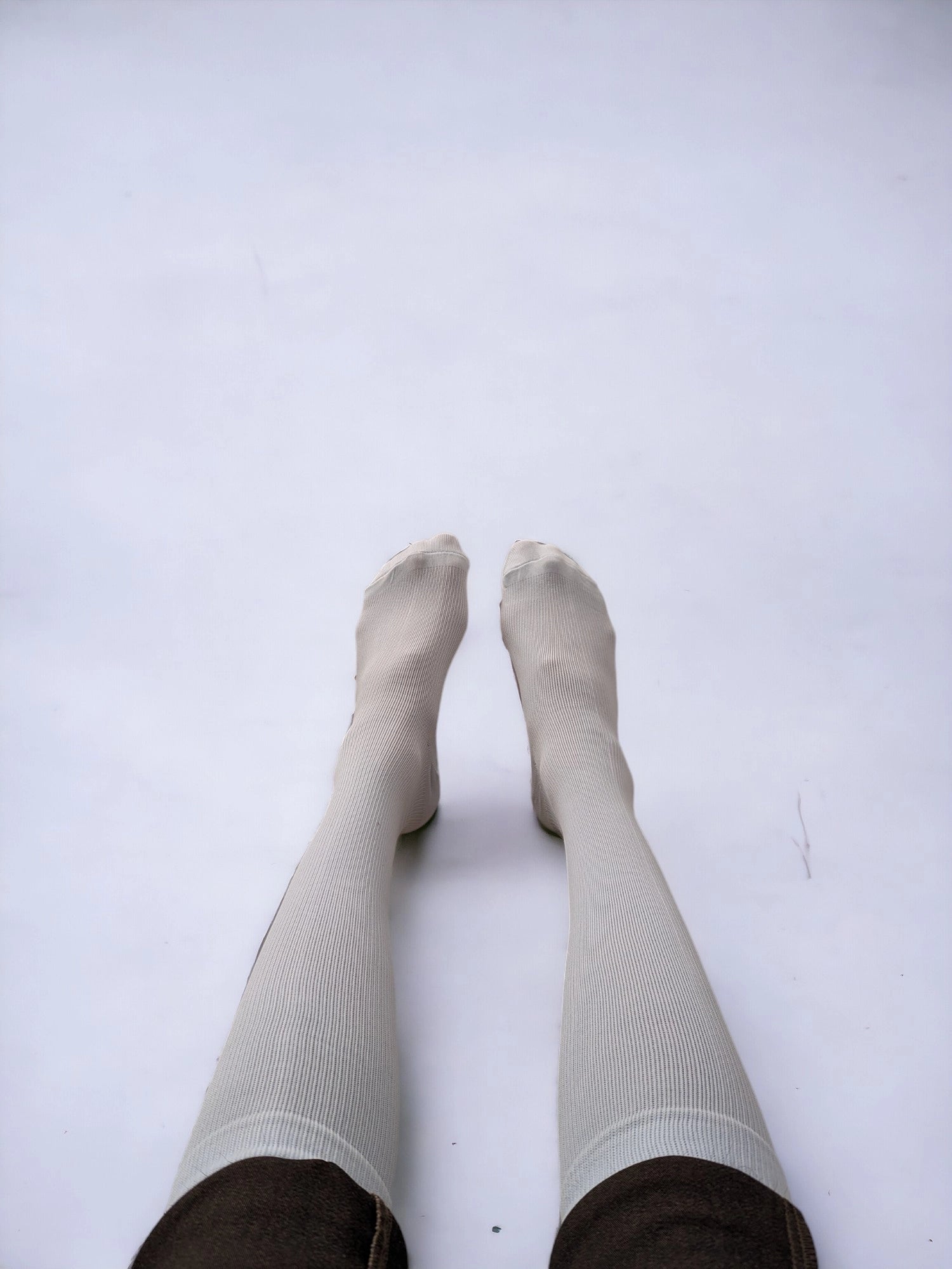 A pair of legs wearing white compression socks raised upward.