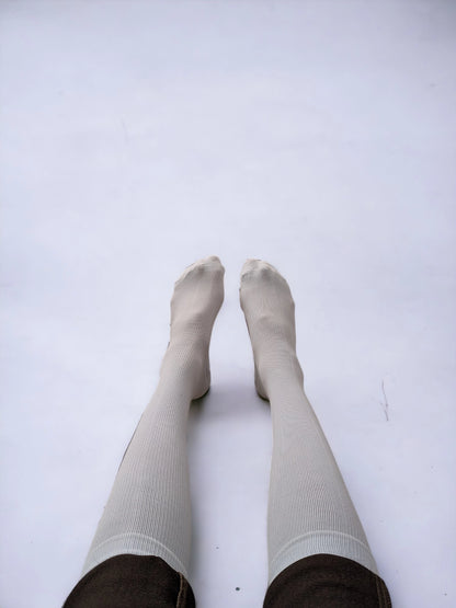 A pair of legs wearing white compression socks raised upward.