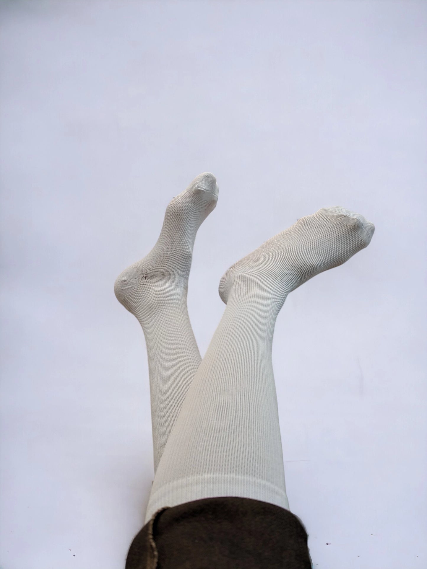 A pair of legs wearing white compression socks raised upward.