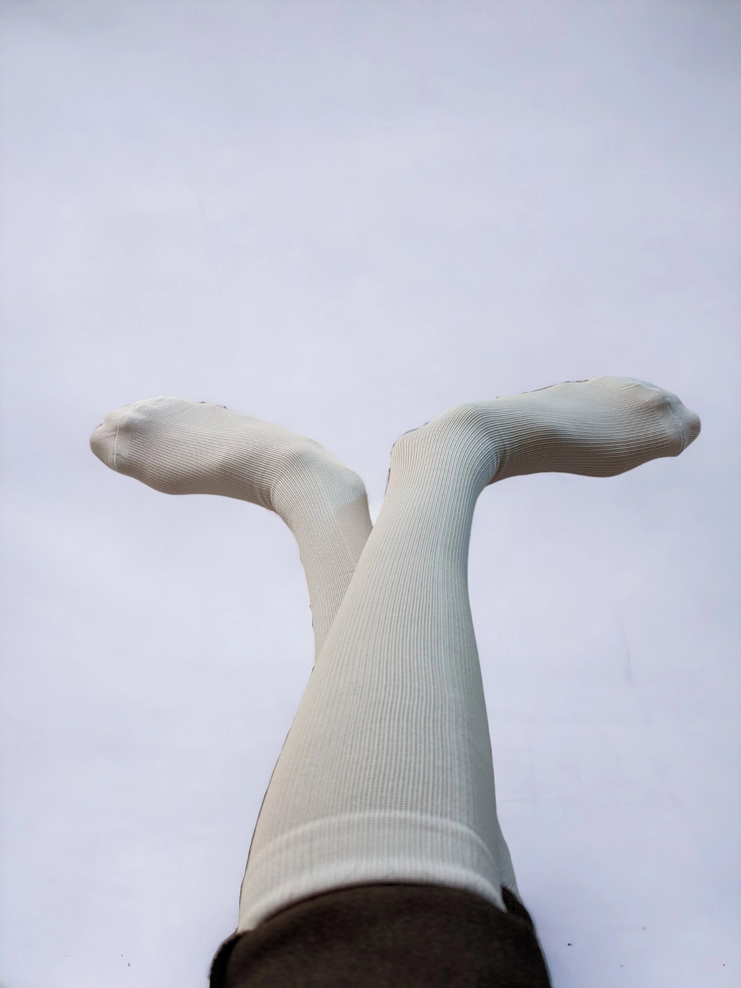 A pair of legs wearing white compression socks raised upward and crossed over each other.