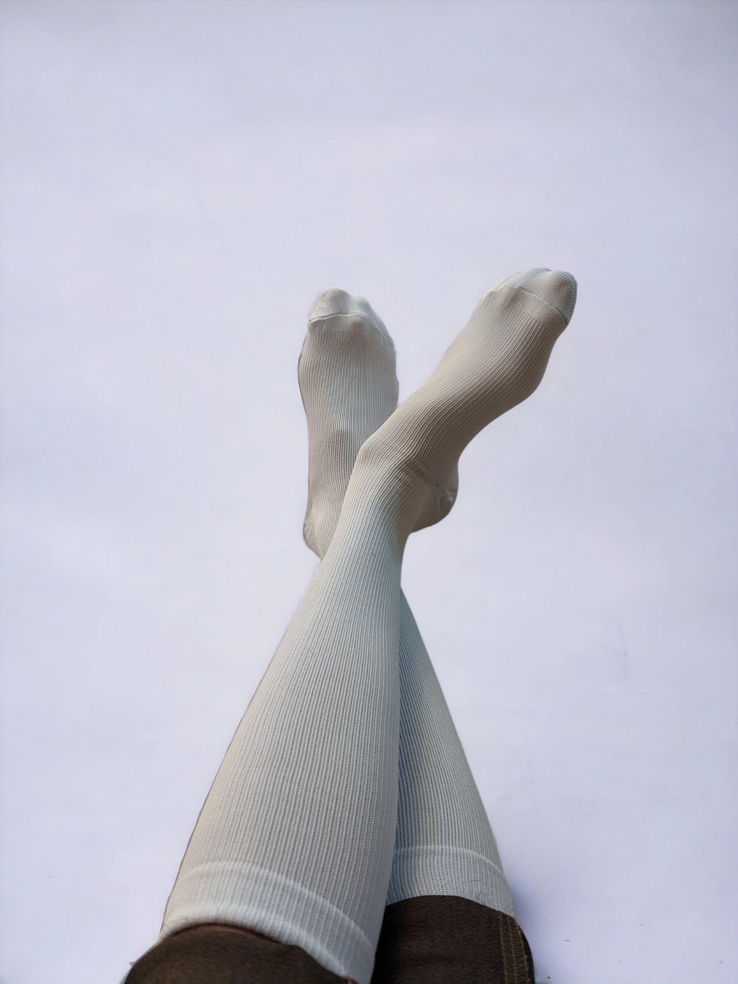 A pair of legs wearing white compression socks raised upward and crossed over each other.
