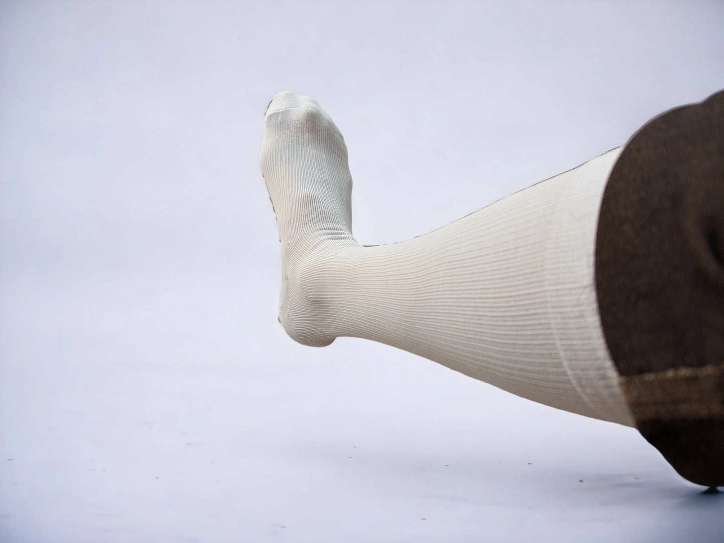 A leg wearing white colored compression socks pointing to left