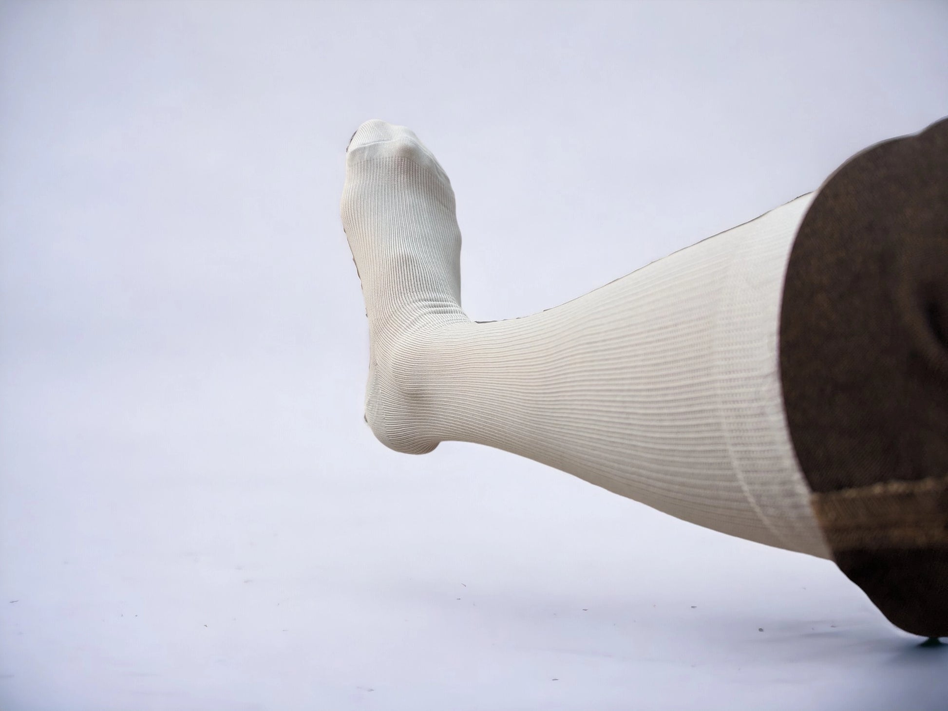 A leg wearing white colored compression socks pointing to left