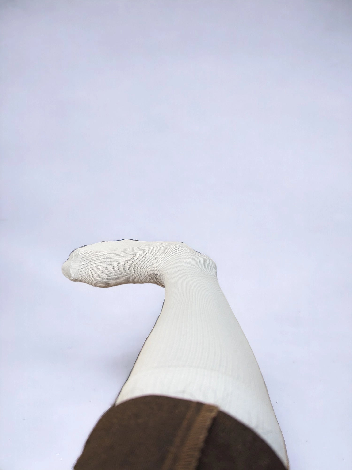 A leg wearing skin-colored compression socks raised upward 